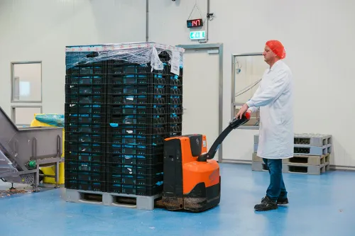 Employee using manual pallet jack with stack of crates of chicken